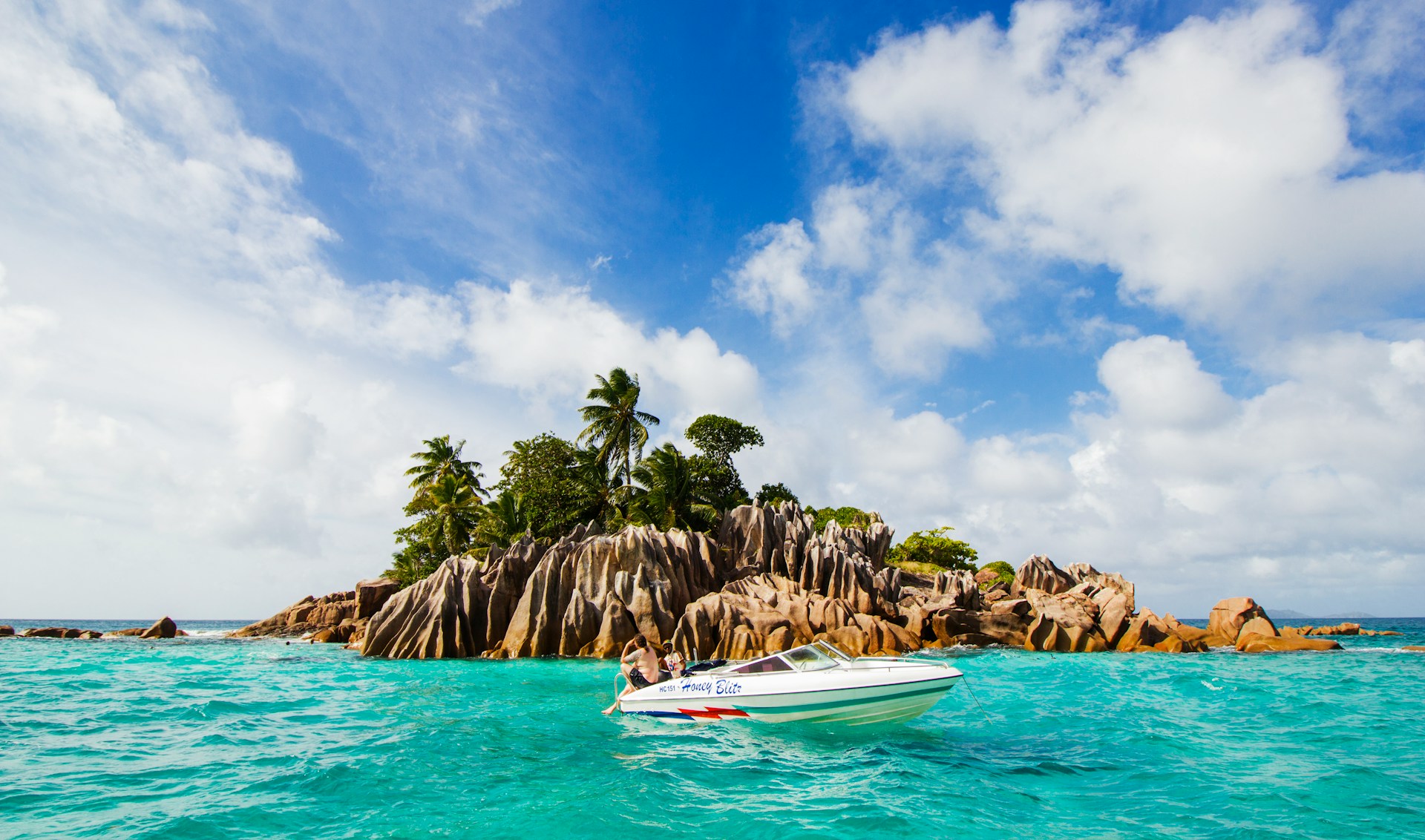 Men on boat surrounded by rock formations and coconut trees in turquoise sea